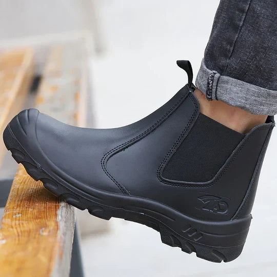 Close-up of a black leather pull-on boot worn with rolled grey jeans, foot resting on a wooden step 1