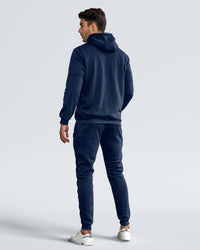 Back view of the navy tracksuit on a model, showing the hood, seamed sleeves and ribbed cuffs 3