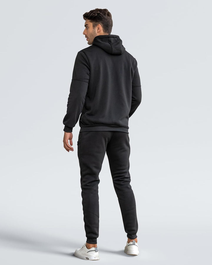 Back view of a man wearing the black hooded jacket and joggers, against a plain grey background 12
