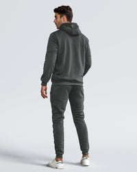 Back view of the dark grey tracksuit on a model, showing hood, seamed sleeves and ribbed hem 5