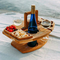 Wooden picnic table on a light blanket holding a blue wine bottle, two glasses, strawberries and cheese 1