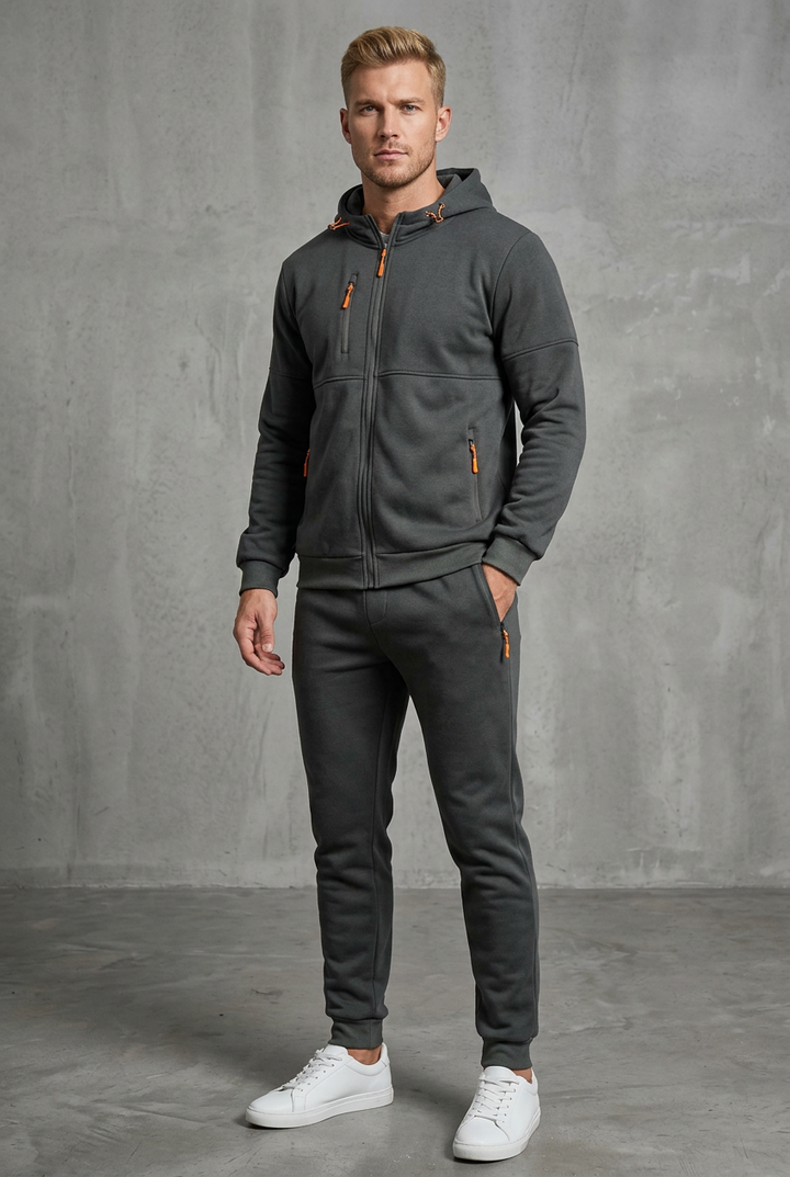 Dark grey hooded zip tracksuit with orange zip pulls, worn by a model, front view, hand in pocket 4
