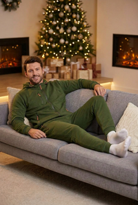 Smiling man relaxing on a grey sofa in a green hoodie and joggers, Christmas tree behind 1