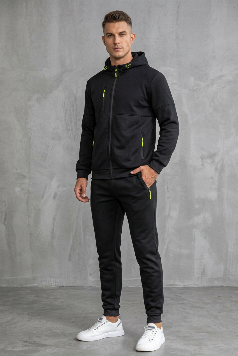 Black hooded zip tracksuit with neon yellow zips, worn by a model, front view against concrete wall 8