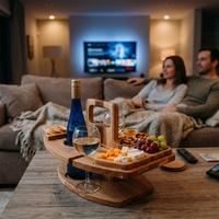 Wooden table holding wine, cheese, grapes and nuts on a coffee table, couple watching TV behind 1