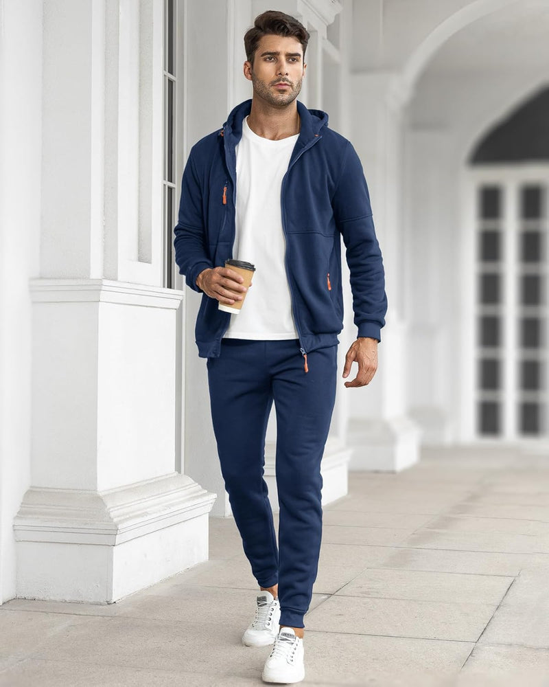 Model walking along a white colonnade in the navy tracksuit with a white tee, holding a coffee 7