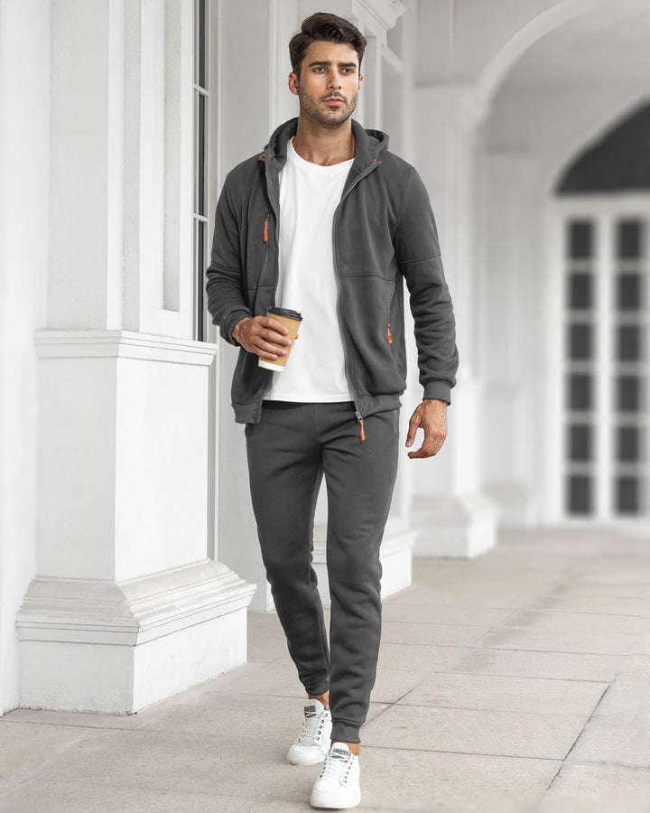 Model walking along a white colonnade in the dark grey set, open jacket over a white t-shirt, holding a coffee 12