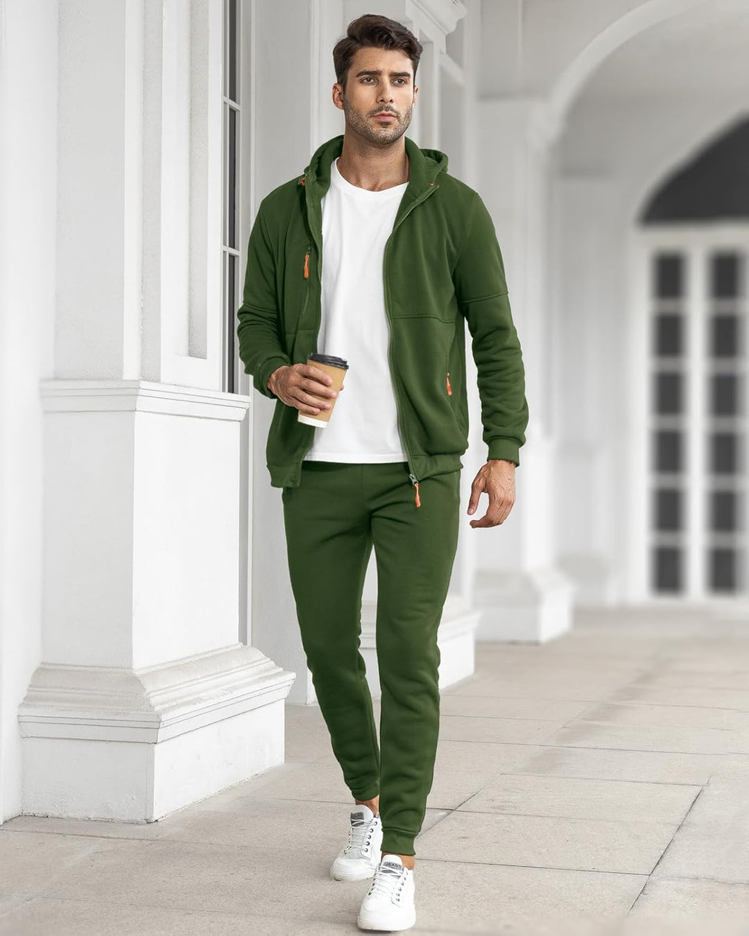 Man in the green tracksuit with the jacket open over a white t-shirt, holding a coffee outdoors 10