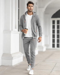 Model walking through a white colonnade in the grey zip-up tracksuit with a white t-shirt, holding a coffee 30