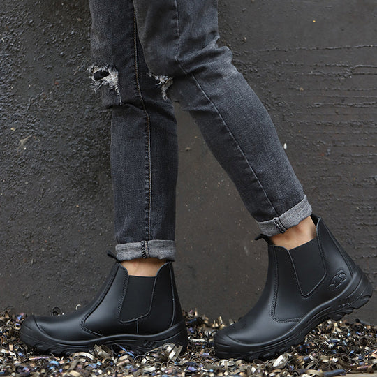 Model in grey ripped jeans wearing black pull-on boots, standing on metal shavings against a dark wall 7