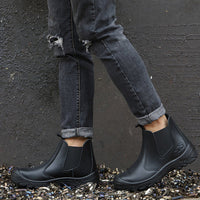 Model in grey ripped jeans wearing black pull-on boots, standing on metal shavings against a dark wall 7
