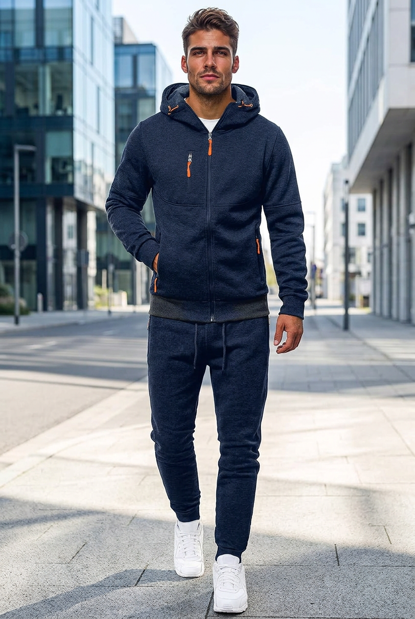 Man in a navy hooded zip jacket and matching joggers with orange zip pulls, walking down a city street 1