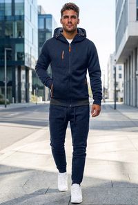 Man in a navy hooded zip jacket and matching joggers with orange zip pulls, walking down a city street 1