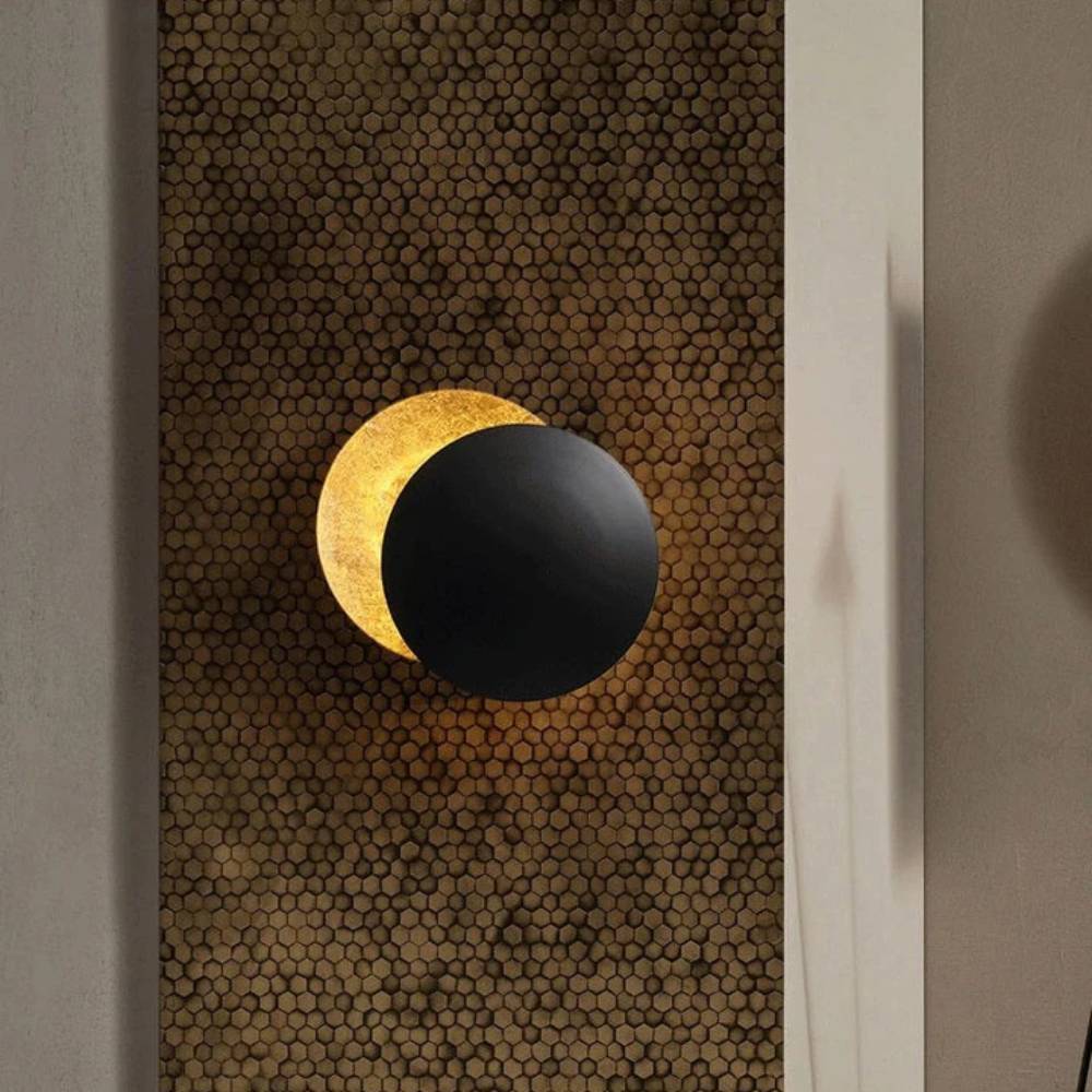 Black disc lamp overlapping a glowing gold disc, mounted on a honeycomb-patterned textured wall panel 1