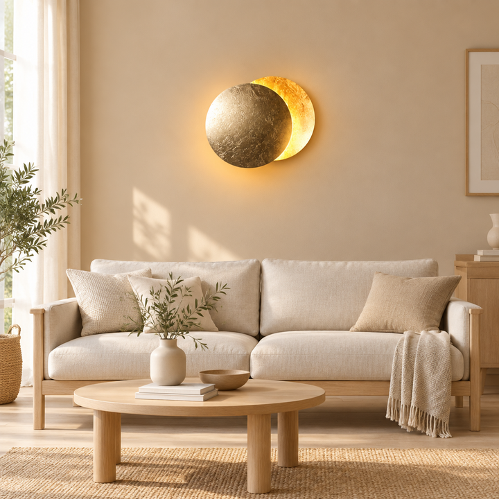 Two overlapping gold-leaf discs glow on a beige living room wall above a cream sofa 1