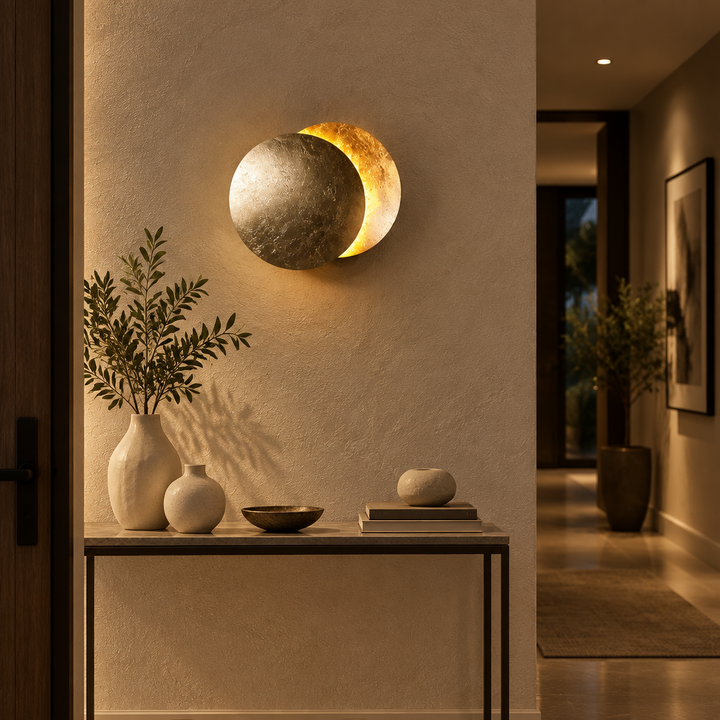 Silver-toned moon wall lamp glowing gold above a console table with vases and a bowl 1