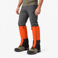 Angled side view of a model wearing orange and black gaiters over hiking boots with a black buckled instep strap 4