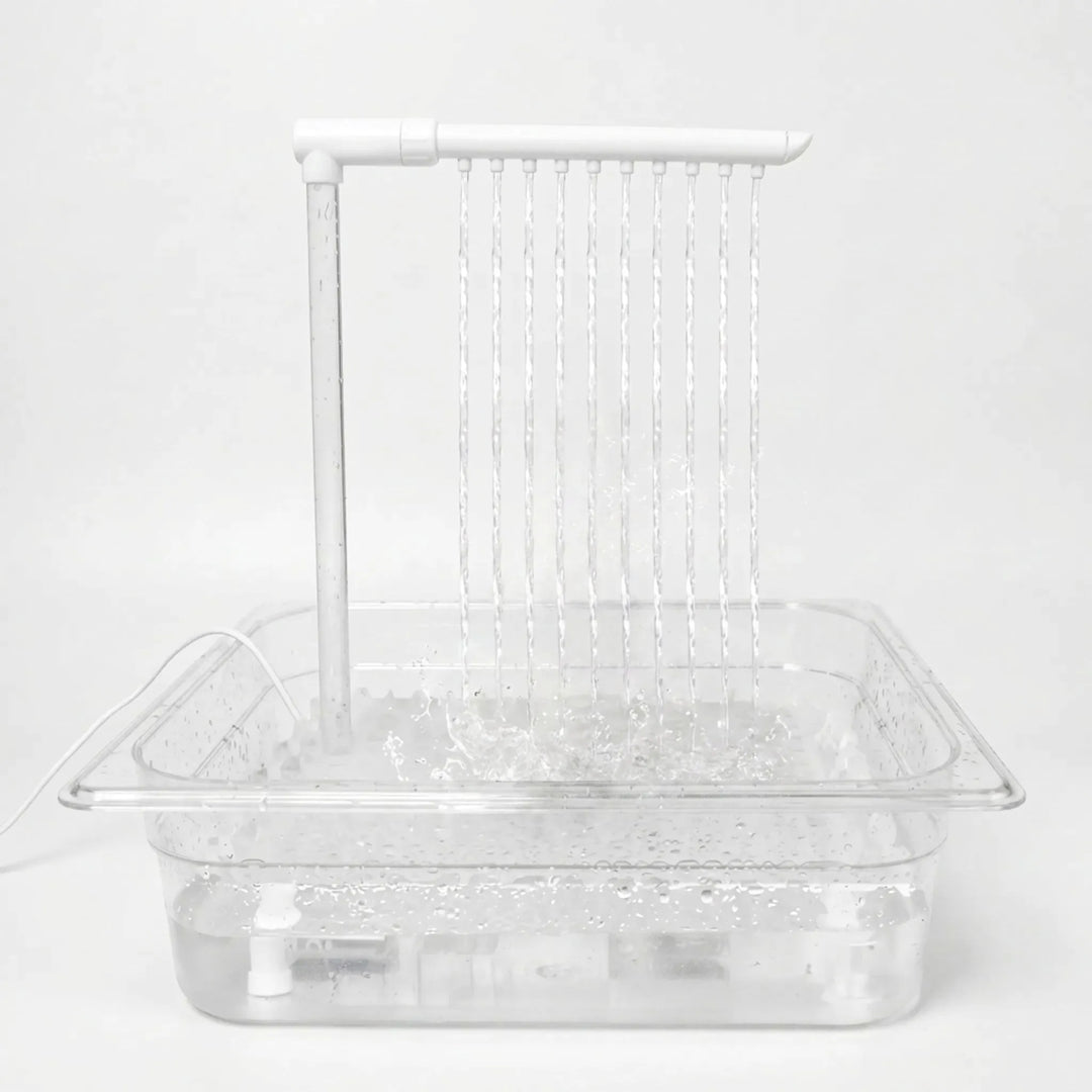 Clear tray filled with water on a plain white background, with a white overhead arm releasing ten thin streams that splash below. 1