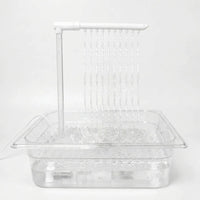 Clear tray filled with water on a plain white background, with a white overhead arm releasing ten thin streams that splash below. 1