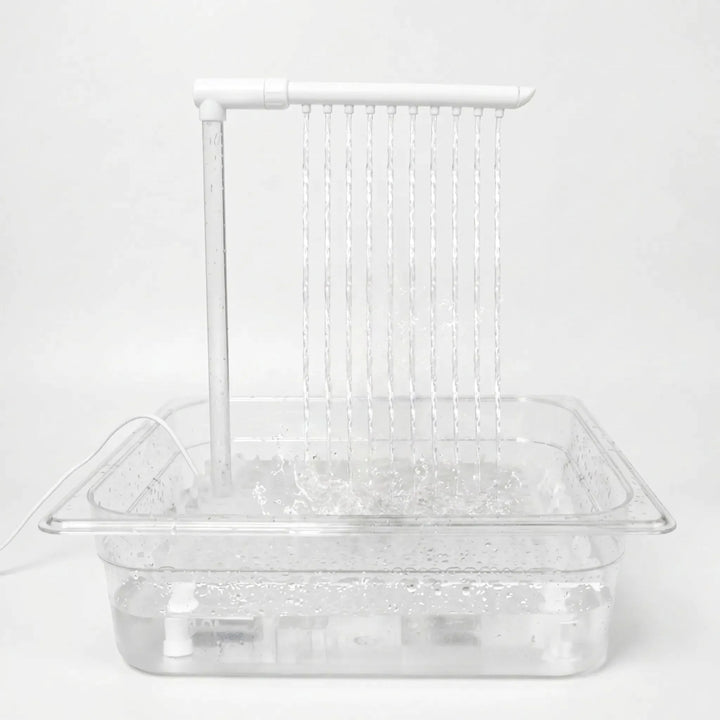 Clear tray filled with water on a plain white background, with a white overhead arm releasing ten thin streams that splash below. 1