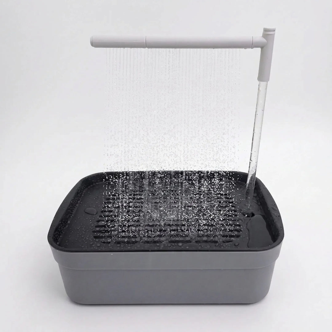 Grey bird bath on a plain white background with water falling from an overhead spray arm onto the slatted tray. 1
