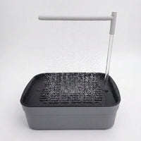 Grey bird bath on a plain white background with water falling from an overhead spray arm onto the slatted tray. 1