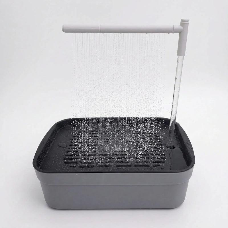 Grey bird bath on a plain white background with water falling from an overhead spray arm onto the slatted tray. 1