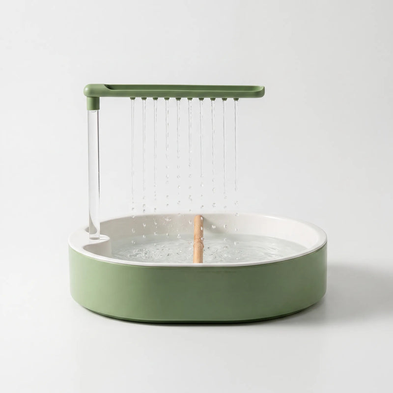 Green and white round bird bath on a plain background, water falling from a row of spouts onto a wooden perch. 1