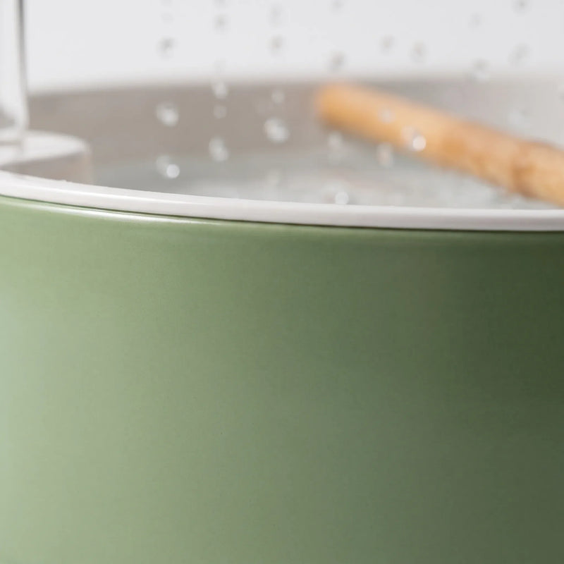 Close-up of the matte green outer wall and white rim of the bath, with blurred water drops and wooden perch behind. 4