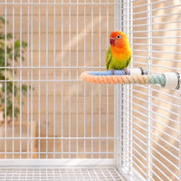 Small green and orange lovebird perched on the pastel rope bent into a curve, fixed inside a white wire cage. 2