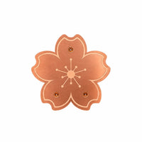 Top view of the copper-coloured blossom-shaped disc on a white background, showing five petals, an engraved stamen pattern and three small rivets. 1