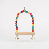 Arched bird swing of multicoloured wooden beads with a natural wooden perch and two small gold bells, on white. 1