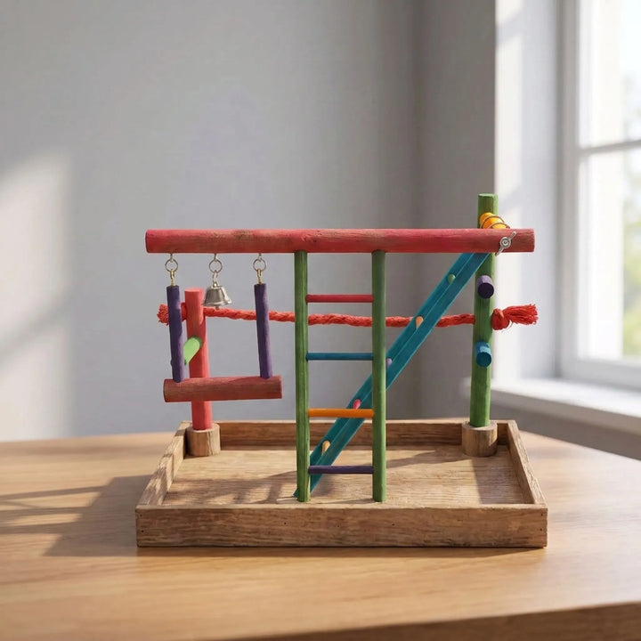 Brightly coloured wooden bird play stand with swing, bell and ladder on a wooden table beside a sunlit window. 2