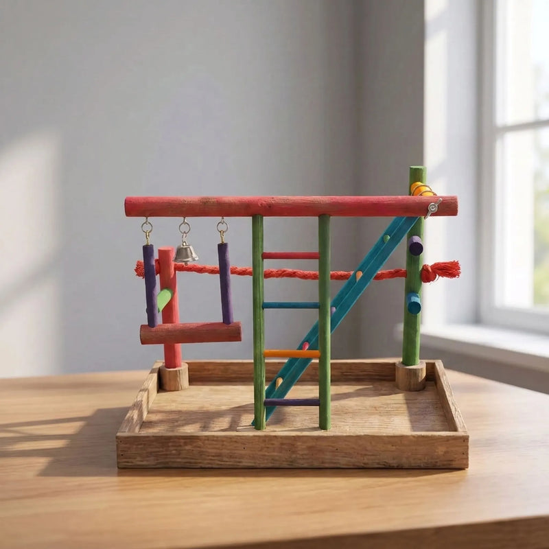 Brightly coloured wooden bird play stand with swing, bell and ladder on a wooden table beside a sunlit window. 2