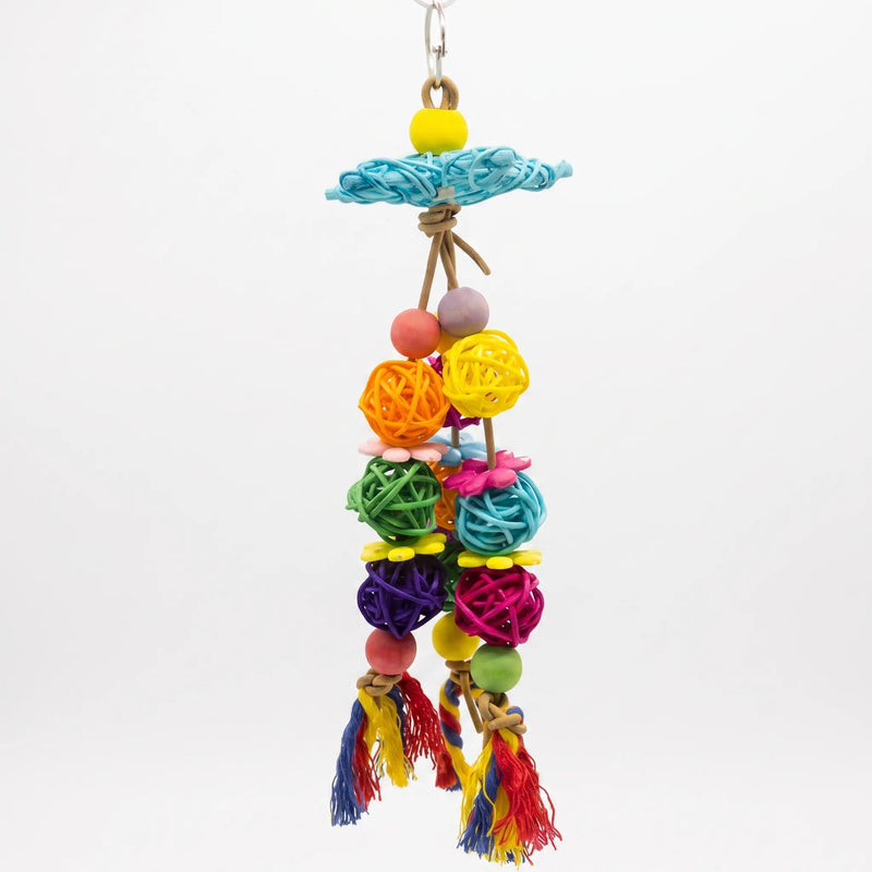 Hanging bird toy against a plain white background, with woven balls in many colours, wooden beads, flowers, a blue woven disc and rope tassels. 1