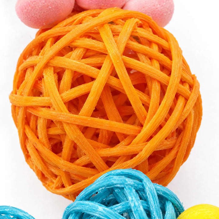 Close-up of an orange woven ball with pink flower pieces above and blue woven balls below, showing the loose weave. 3