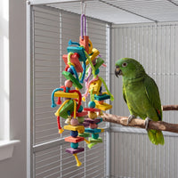 Toy hung vertically from a metal clip inside a cage, with a green parrot perched on a branch beside the dangling blocks and ropes. 3