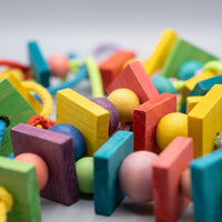 Close-up detail of the dyed wooden blocks and round beads threaded on rope, showing the wood grain and bright colours. 4