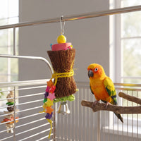 Hourglass-shaped fibre bird toy with a yellow bead, star beads and a bell hangs in a cage beside a perched sun conure. 1