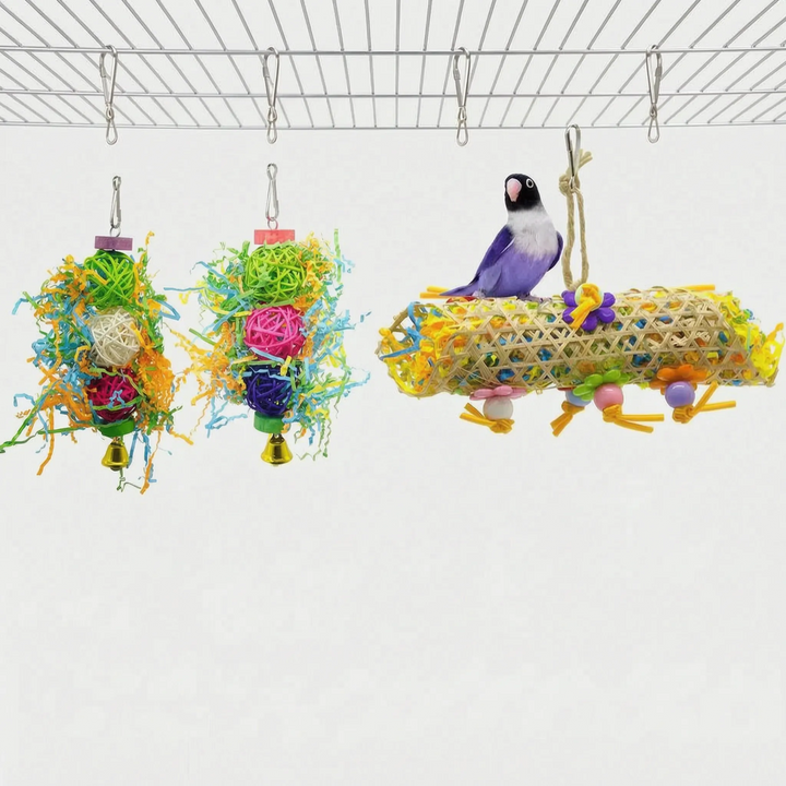 Two rattan ball shredding toys with paper strips and bells beside a woven cane tube with a lovebird perched on top. 6