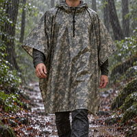 Hooded camouflage poncho in a grey digital pattern worn by a man walking along a rainy forest trail. 1