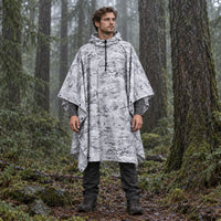 Model wearing the hooded poncho in a white and grey snow camouflage pattern, standing in a misty evergreen forest. 3