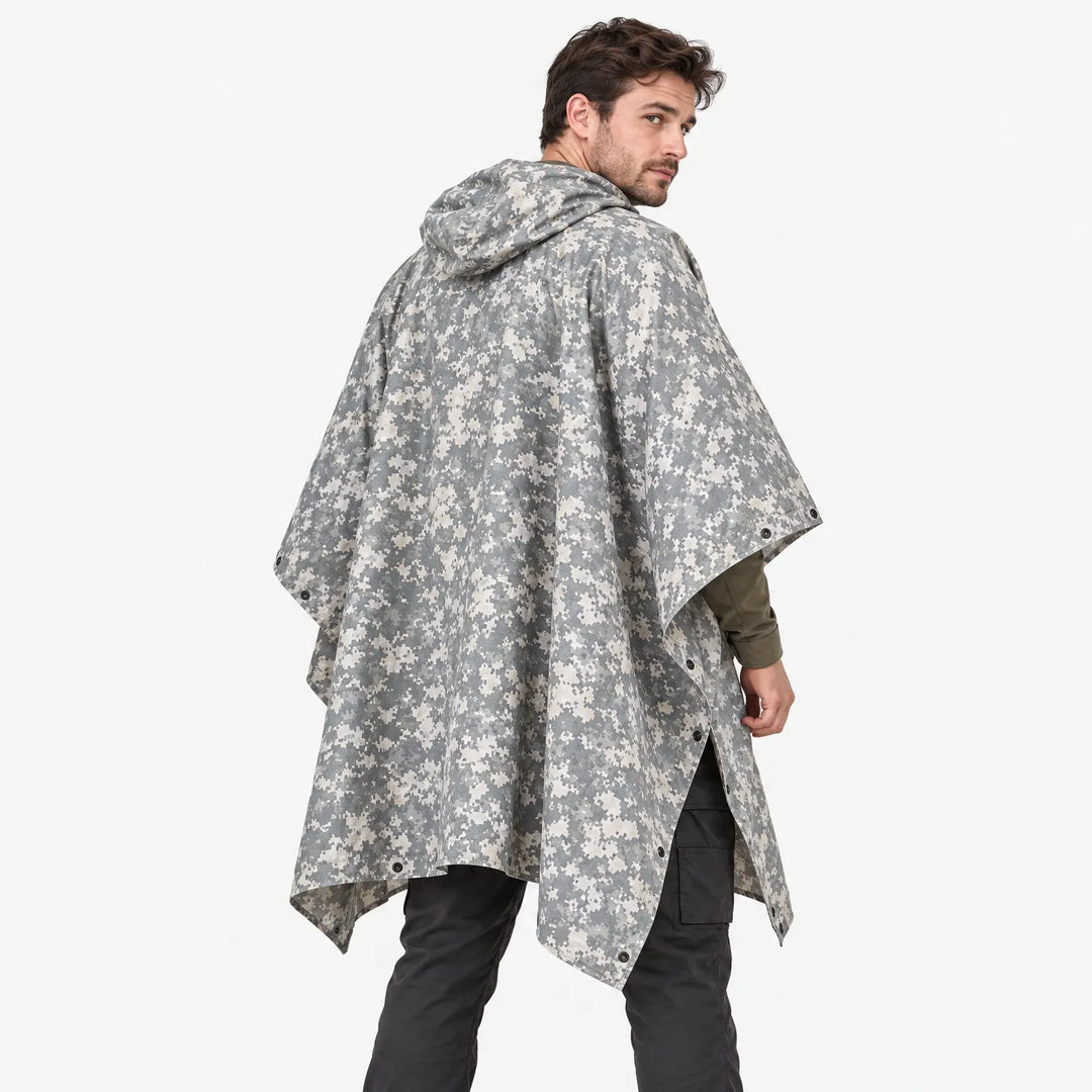 Back view of the poncho in grey and beige digital camouflage, model glancing over his shoulder, snap fasteners along the sides. 4