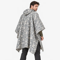 Back view of the poncho in grey and beige digital camouflage, model glancing over his shoulder, snap fasteners along the sides. 4