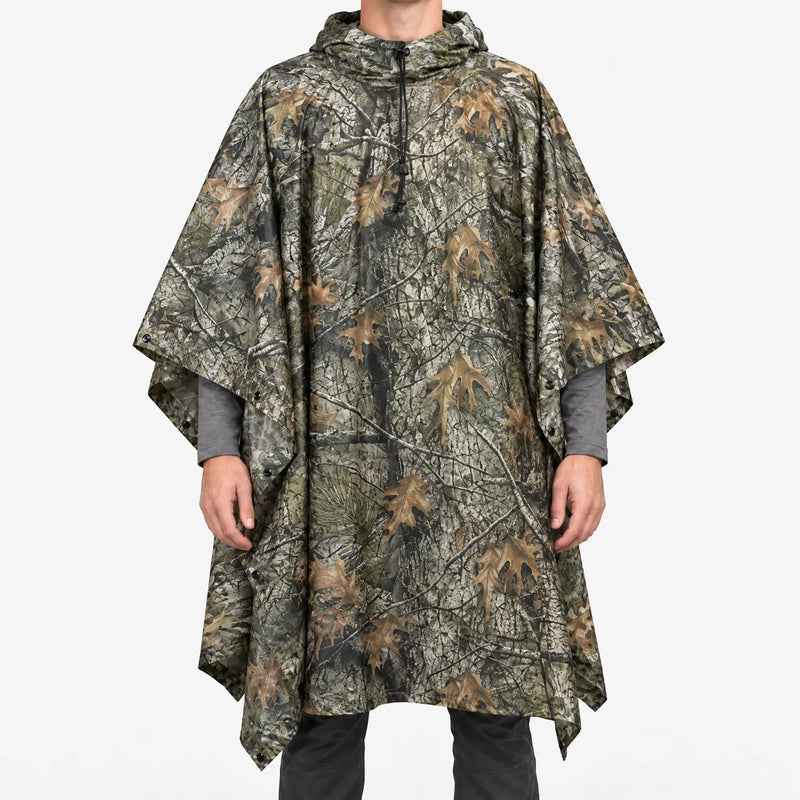 Front view of the hooded poncho in a woodland tree-bark and oak leaf camouflage pattern on a model against white. 9