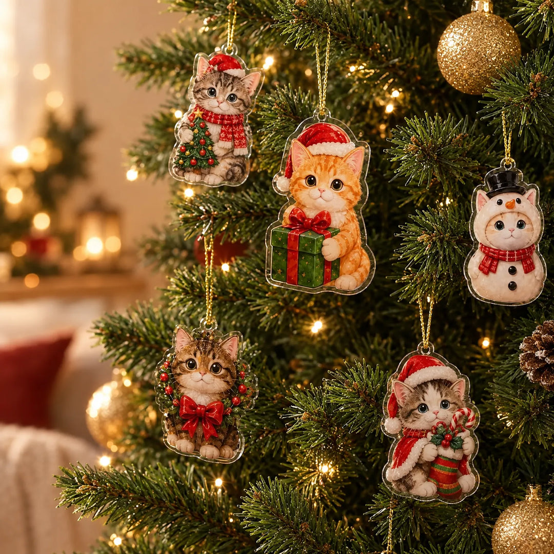 Five clear acrylic cat ornaments in festive outfits hanging on gold cords from a lit Christmas tree with gold baubles. 1
