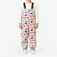 Child in white dungarees printed with pink, red and yellow dinosaurs, volcanoes and palm trees on a faint grid background. 11