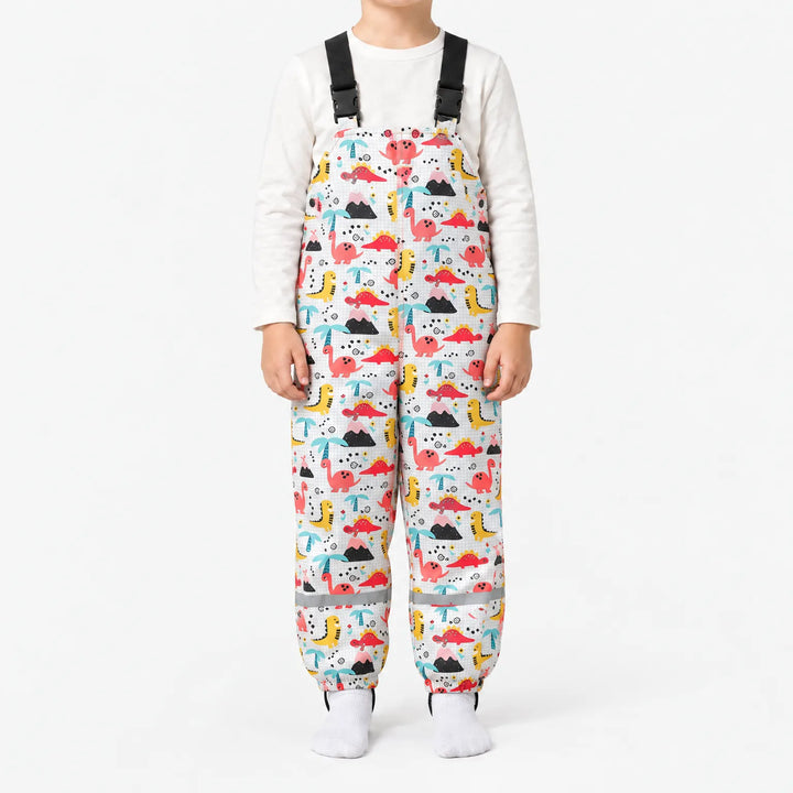Child in white dungarees printed with pink, red and yellow dinosaurs, volcanoes and palm trees on a faint grid background. 11
