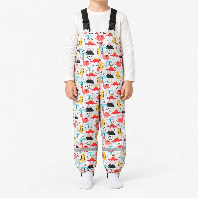 Child in white dungarees printed with pink, red and yellow dinosaurs, volcanoes and palm trees on a faint grid background. 11