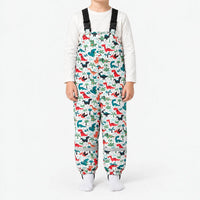 Front view of white dungarees with a pattern of red, teal and black dinosaurs among palm trees, worn with a white top. 12